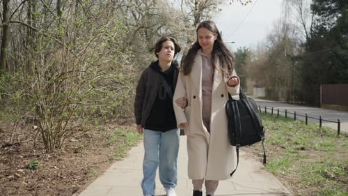 A moody teenager complains to his smiling mother during a playful family walk
