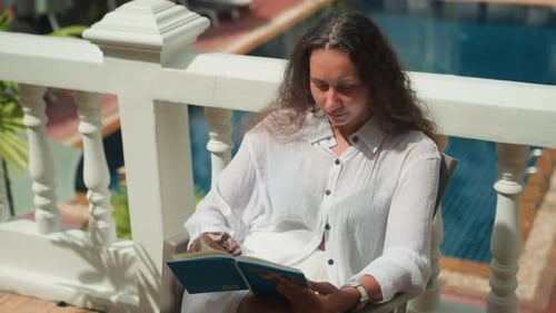 Woman Immersed in Reading at Sunny Island Balcony Female Reader in Elegant Attire Relaxing on Island