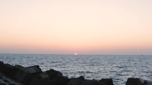 Sunset Over Calm Ocean Water Near Rocky Beach