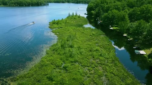 4k drone video of a lake canal in the summertime with a pontoon boat moving across the blue water on