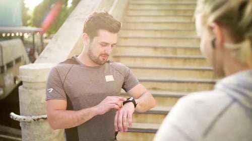 Young Couple Runners Standing by the Stairs in the City Using Smart