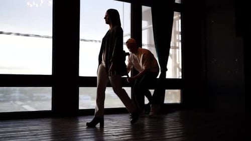 Videographer with camera on gimbal film model walk near bright studio window