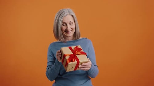 Senior Woman Smiling Holding Gift on Orange Background