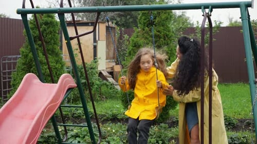 Mutter schiebt ihre Tochter freudig auf eine Schaukel auf dem Spielplatz im Hinterhof
