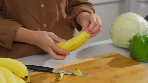 Woman peels and cuts a banana in a kitchen