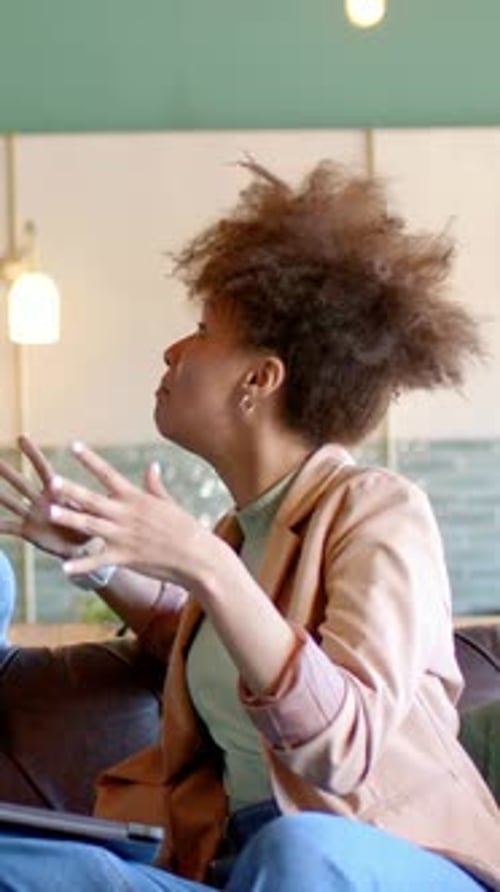 Vidéo verticale : une femme en blazer faisant des gestes mettant l'accent sur un point dans le salon avec une tablette après l'invite de ses pairs