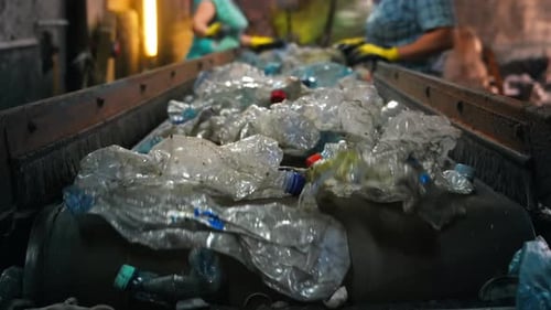 Plastic garbage on a conveyor belt at waste recycling factory. Workers on the background