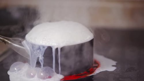 Une casserole de lait sur une cuisinière bout, tandis que de la vapeur s'échappe et que le lait bouillonne et colle à la surface