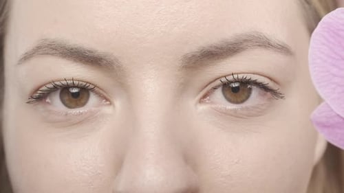 Orchid Flowers Cover Woman's Eyes Close Up The Woman Removes the Flowers and Looks Straight Ahead