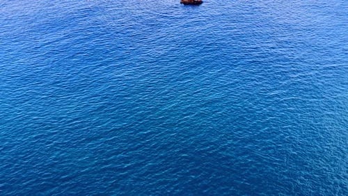 Rocher unique dans une eau bleue largement ouverte. Une petite pierre isolée brise la surface
