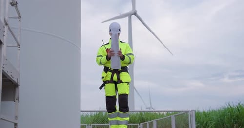 Caucasian engineer standing beside turbine holding blueprint reviewing renewable energy
