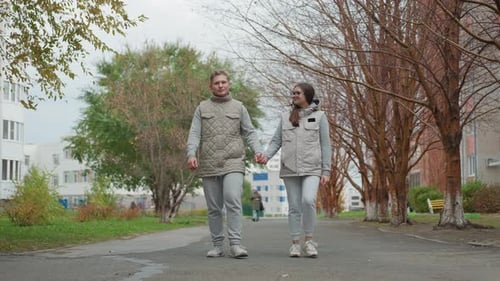 Couple Strolling Hand in Hand Outdoors in Matching Outfits Along Treelined Path