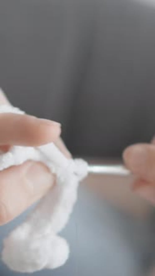 Hands crocheting a piece of white yarn