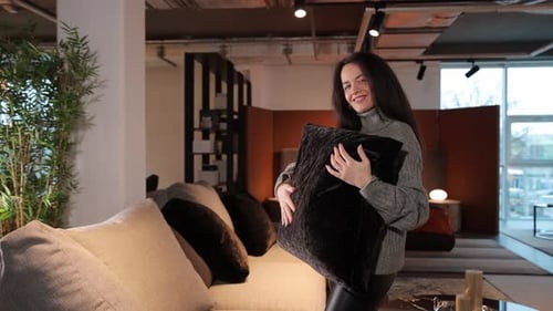 Portrait of Beautiful Smiling Woman Holding Couch Cushion While Posing in Furniture Showroom