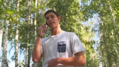 Un jeune homme parle au téléphone en se promenant parmi les bouleaux avec la lumière du soleil