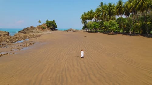 Woman in white walking alone on vast brown sand beach Playa Perfecto Costa Rica