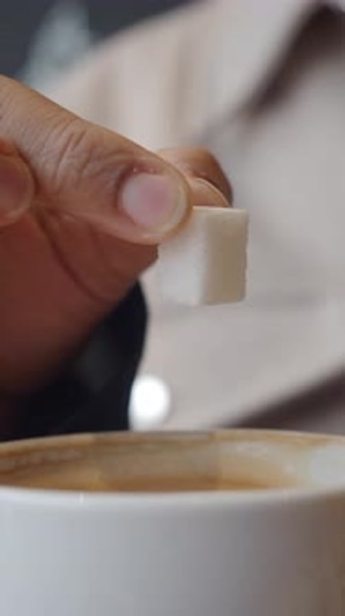 Adding Sugar to a Warm Beverage in a Cozy Cafe Setting