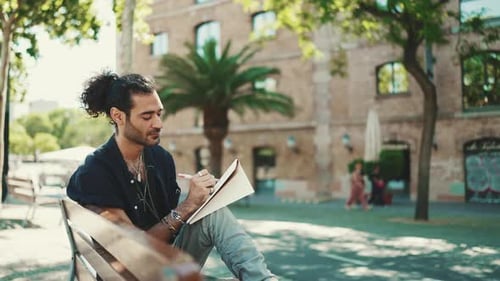 Man Sits on Bench Drawing in Notebook