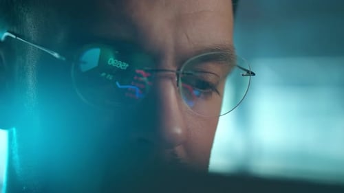 Trader Wearing Glasses is Working on Laptop Computer Screen with Stock Market Charts and Bitcoin BTC