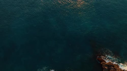 Waves hitting the rocky shore. Drone flight above the dark blue waterscape of the Pacific Ocean