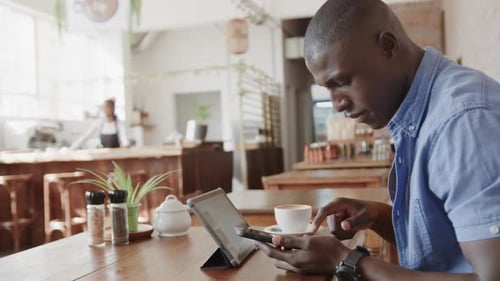 African american man using tablet and smartphone at coffee shop, slow motion