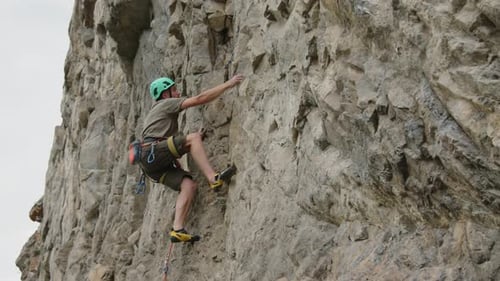 Alpinist Climbing Up Steep Rock with Rope and Using Chalk for Hands