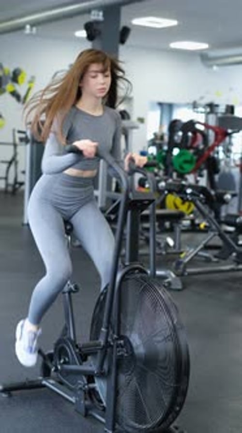 A Young Woman Doing Cardio on a Crossfit Bike Training in the Gym on an Air Bicycle Vertical Video