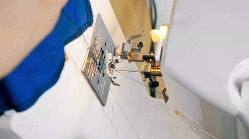 Vertikale Video-Nahaufnahme in einer Nähwerkstatt auf einer Maschine, die Schneiderin macht einen Schnitt auf einem Blau