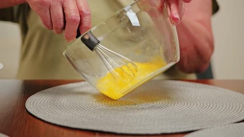 Oma verquirlt Eier langsam in einer Glasschüssel, Nahaufnahme einer traditionellen Kochbewegung