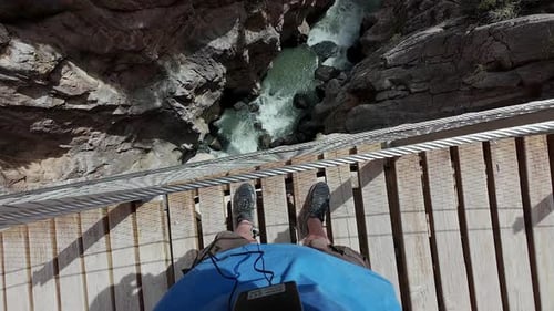 Man explores standing on top of bridge with metal railing and tall drop off to see downcut valley