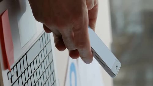 Hand Holds Phone Over Laptop Near Data Chart