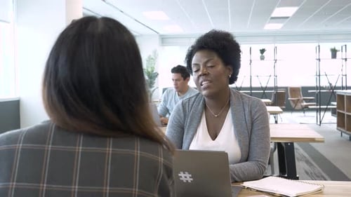 Businesswomen collaborate face to face at laptop in modern coworking space office