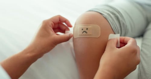 Adult Applies Bandage with Sad Face to Knee