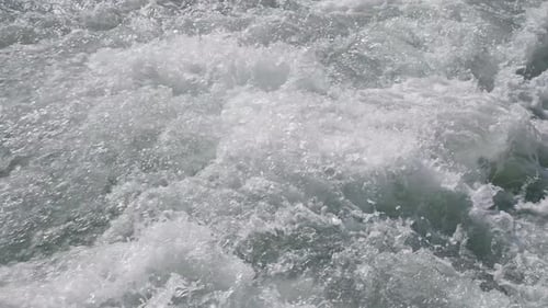 Wasserspritzer in einem Gebirgsfluss mit schneller Strömung unter strahlender Sonne, Zeitlupen-Nahaufnahme