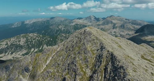 Rocky mountain tall peak surrounded by mountain ranges, on a clear sunny day with blue skies, drone