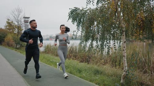 Energetic Young Couple in Sportswear Enjoys Outdoor Jogging in a Park Embodying Health and
