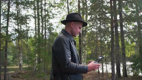 Caucasian model operating a drone in the forest and looking to his device. Wide shot