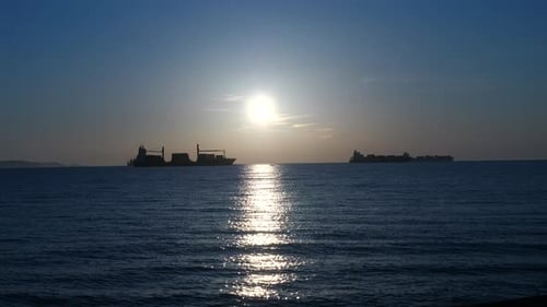 Silhouette of marine transport and tanker ships on open ocean water at sunset