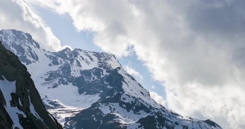 Snow capped mountains reaching towards a blue sky with dramatic white clouds. aerial, timelapse