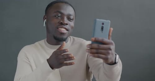 African American Man Making Online Video Call with Smartphone and Earphones Talking Gesturing