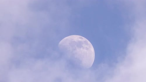 Moon Shines Through Drifting Clouds in Blue Sky