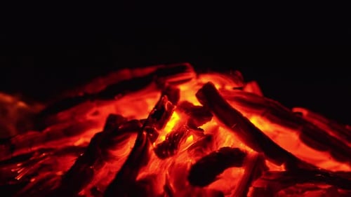 A pile of smoldering embers close up. Little tongues of flame and sparks appear on the coals.