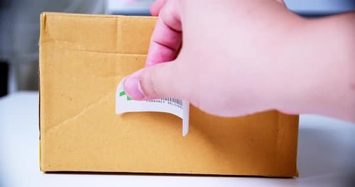 Hände beim Anbringen des +PHARMACY Sticker-Etiketts auf einen Versandkarton