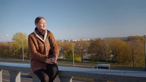 Woman Sits on Bridge Drinking Coffee in City Park