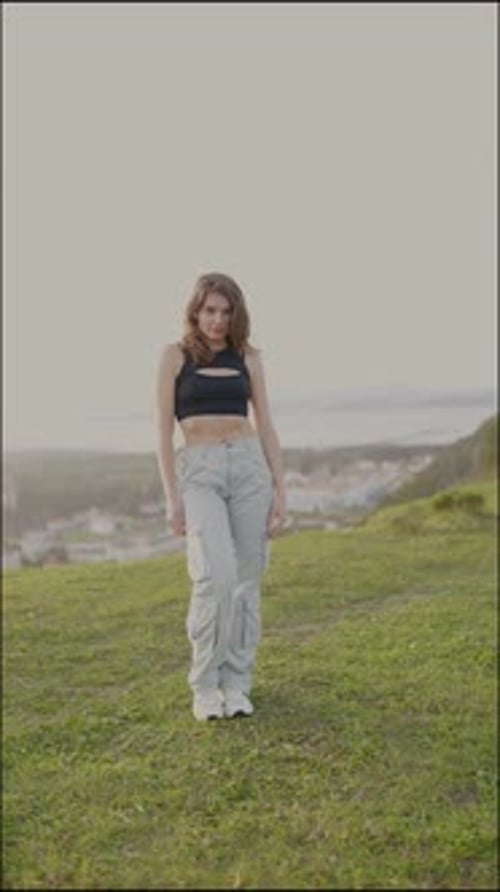 Woman dances in a grassy field near city