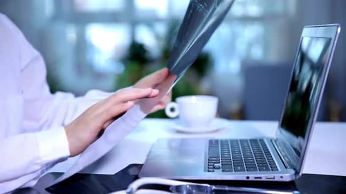 Medical Professional Examining X-ray at Desk with Laptop