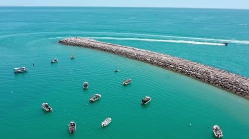 Fischerboote fahren am frühen Morgen durch türkisfarbenes Wasser und passieren einen Steinbrecher