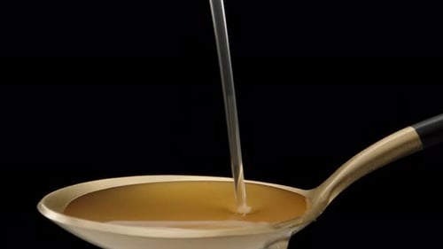I pour yellow syrup on a golden spoon. Dolly slider extreme close-up.