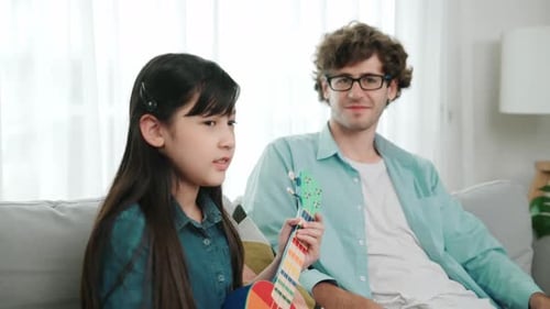Girl singing and playing ukulele with adult at home
