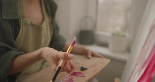 Close Up a Girl in a Green Apron Takes Some Paint From Her Palette and Applies It with a Large Brush